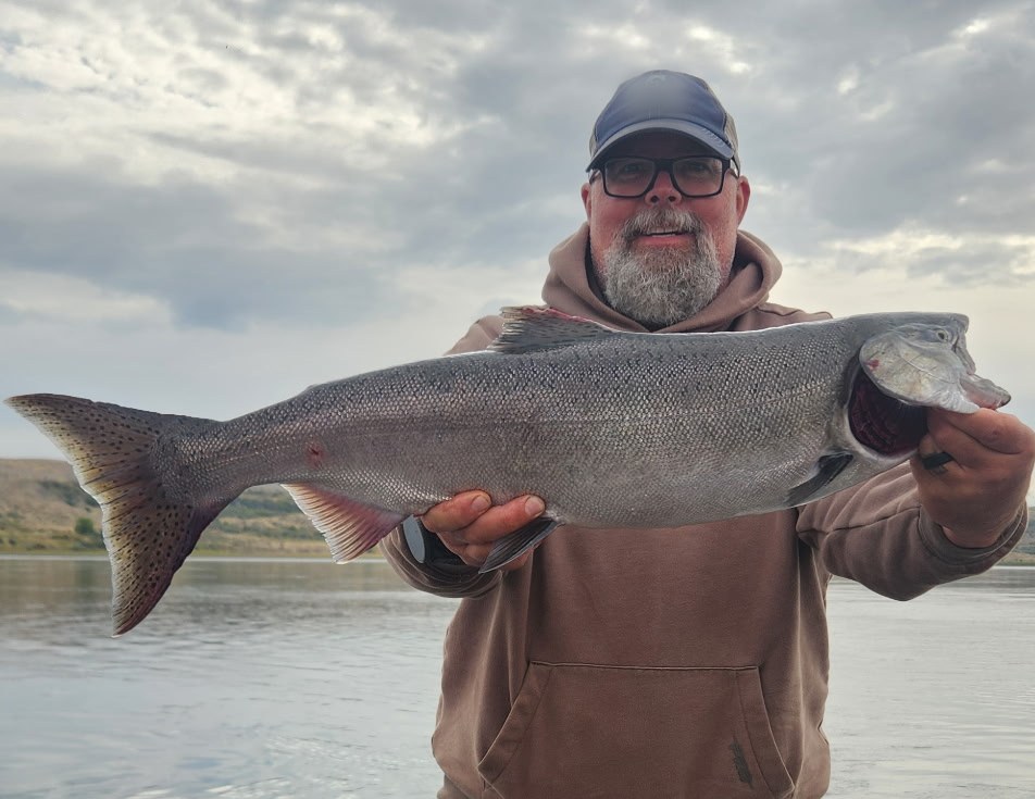 Mike holding a large fall chinook salmon on a boat on a wide river, under a cloudy sky.