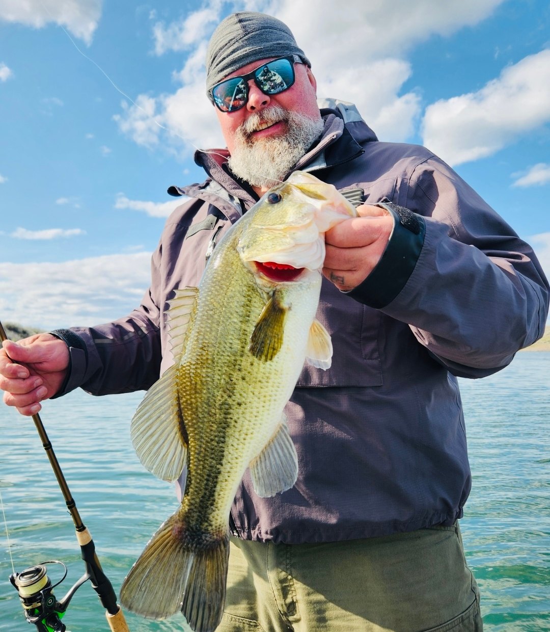 Mike holding a largemouth bass on a boat under a bright sky with scattered cloud.